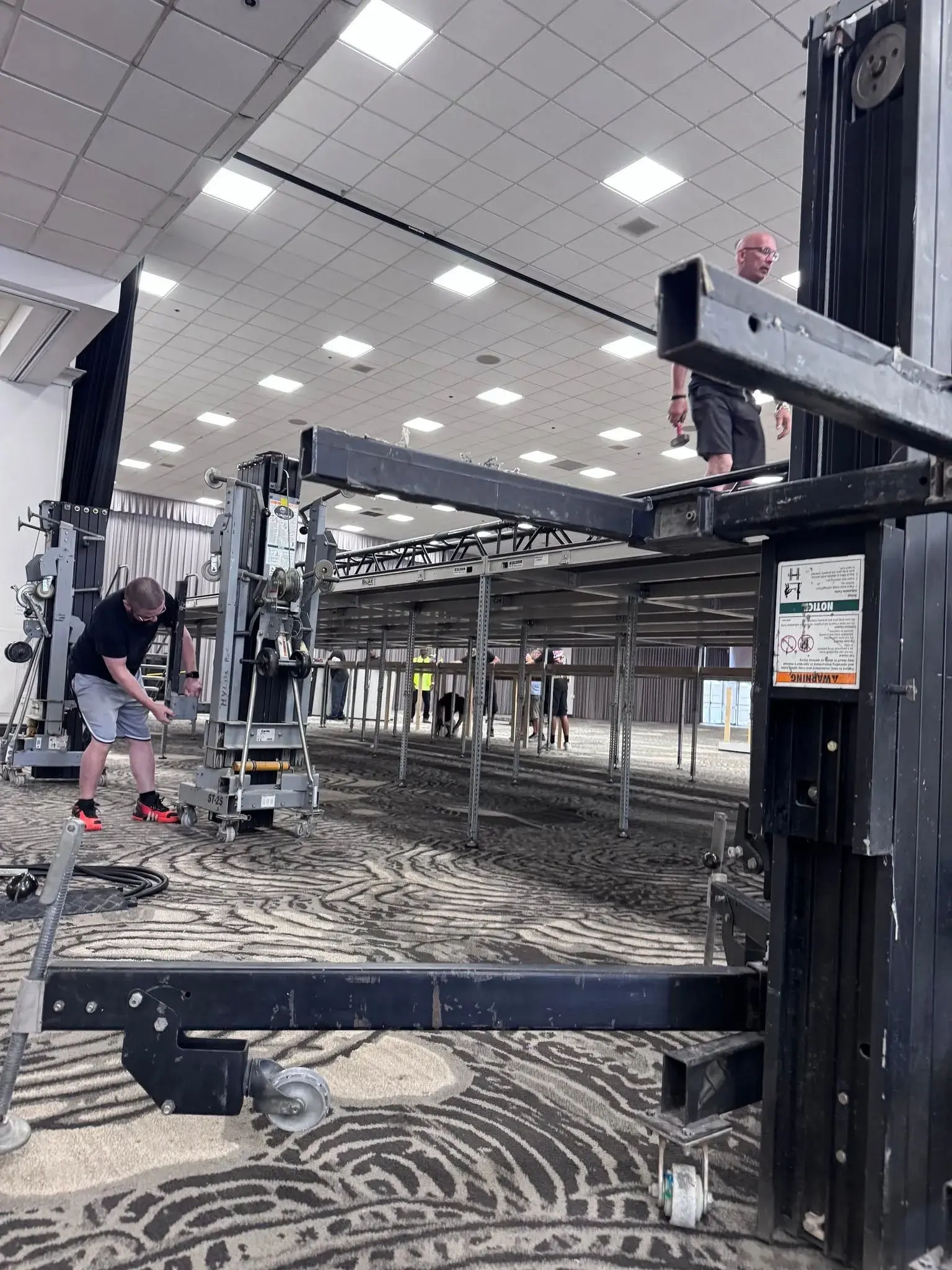 Production crew assembling stage trussing inside a large event venue