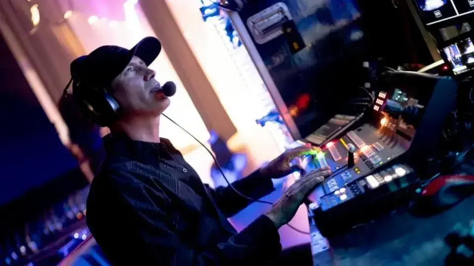Production operator wearing a headset and working at a live video switcher under purple and blue stage lighting
