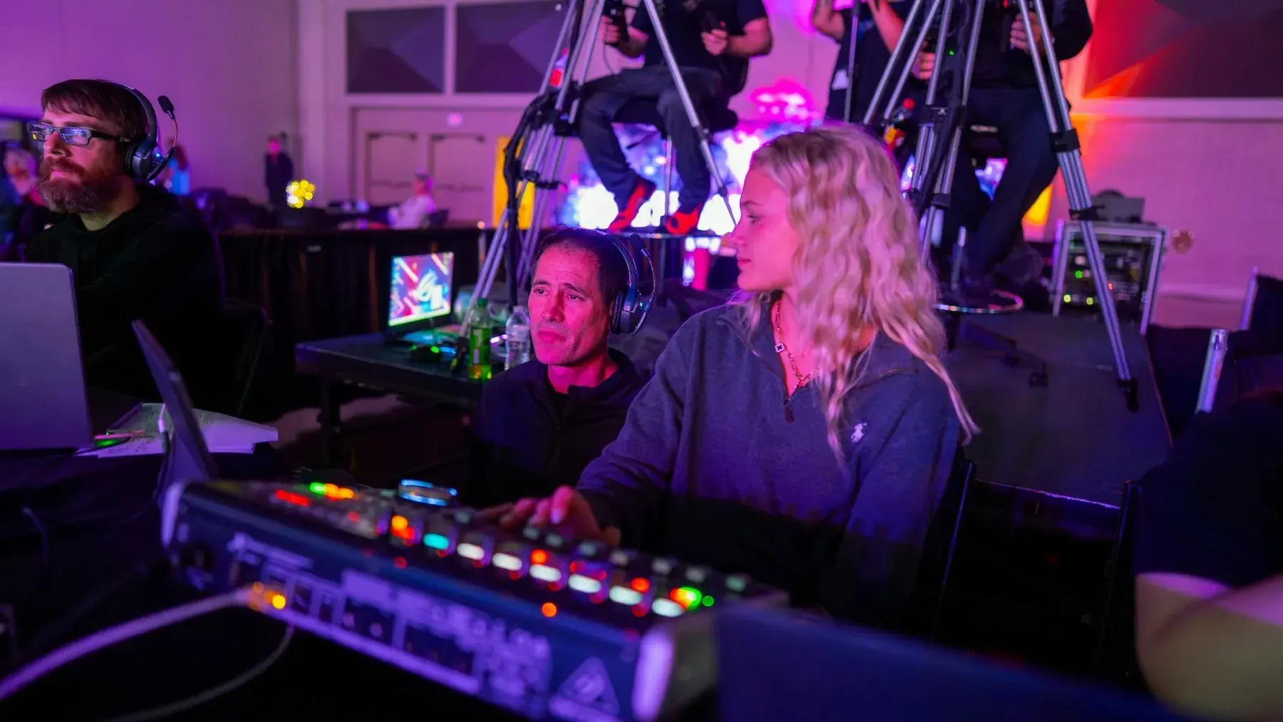 Sound team working at an audio console in a live event environment with cameras and purple stage lighting