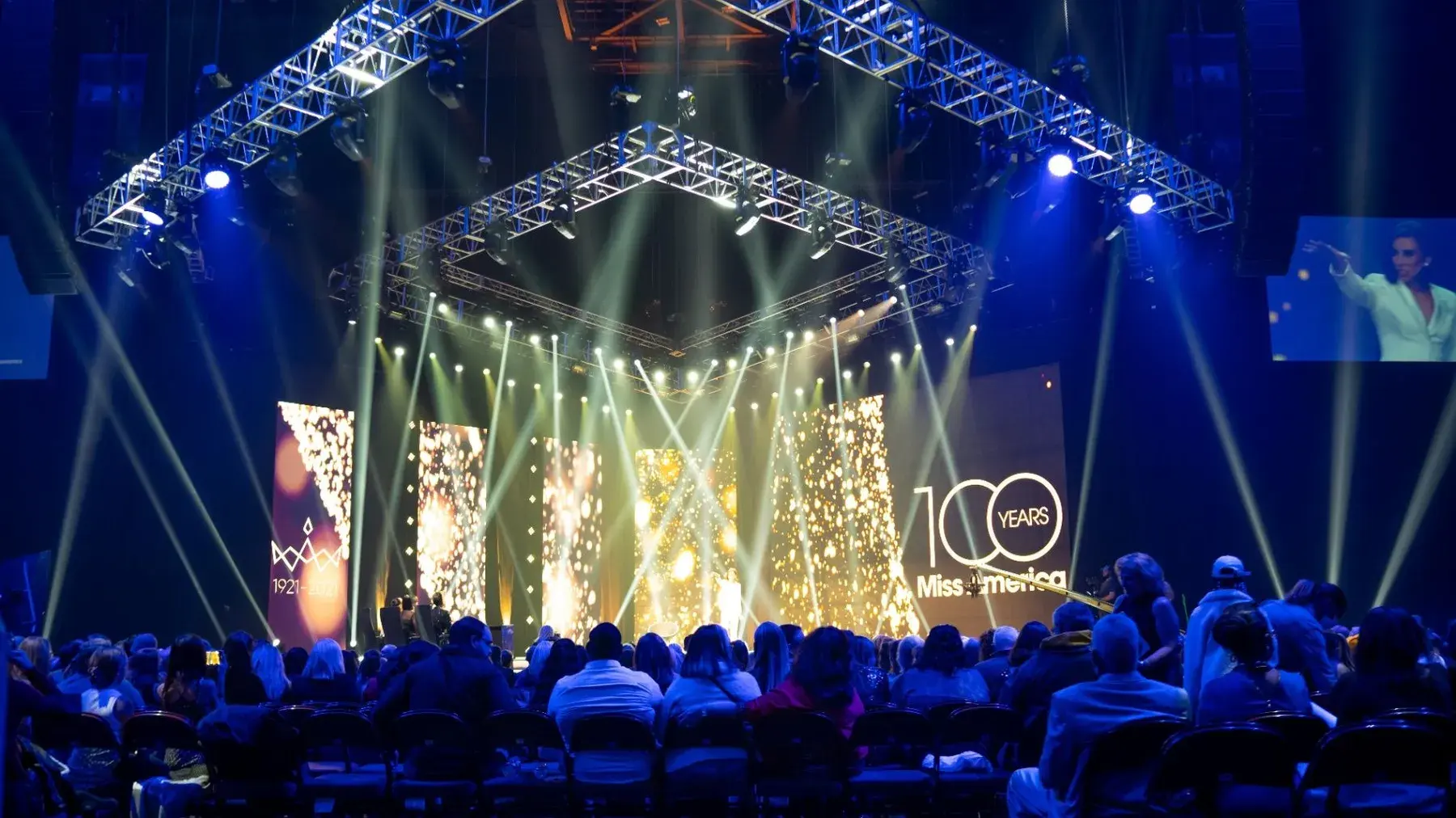 Large stage with video walls, lighting, audience, and overhead truss
